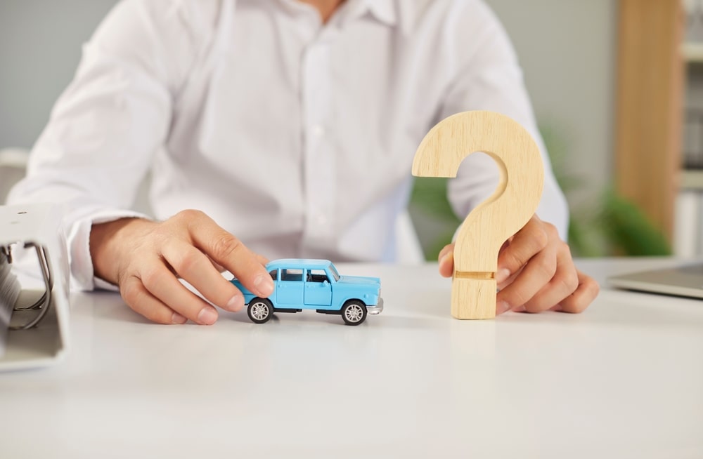 Worker at a desk holds a blue toy car and a wooden question mark