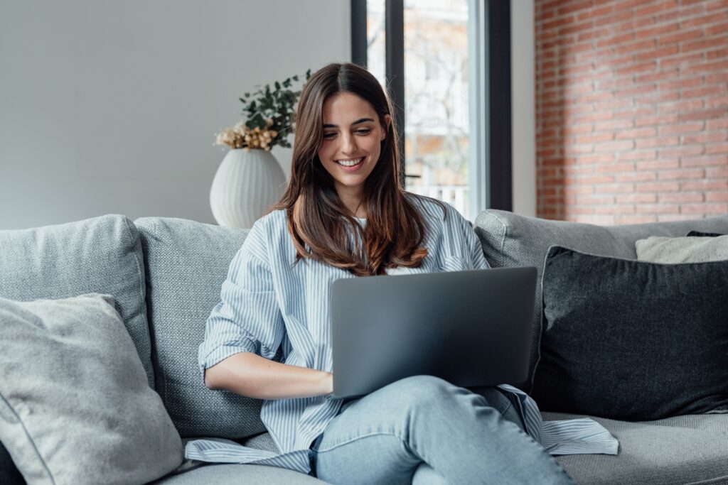 A young woman sitting at a desk, using a laptop to list her car for sale on a vehicle marketplace website