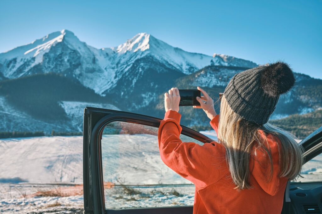 Woman photographing snowy mountains near her car during a winter trip