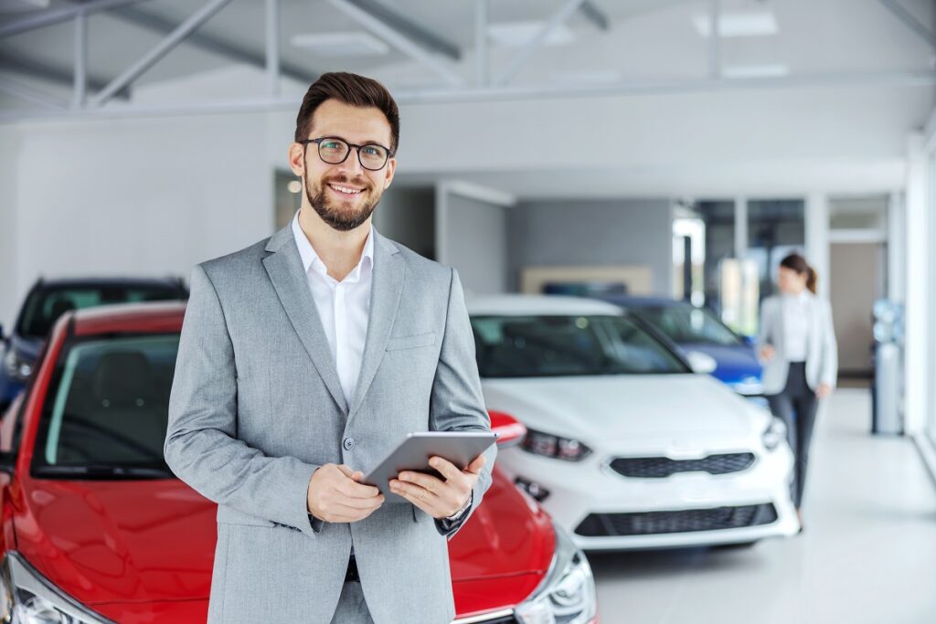 Man with a tablet in a car showroom, focused on Automotive Inventory Management strategies.